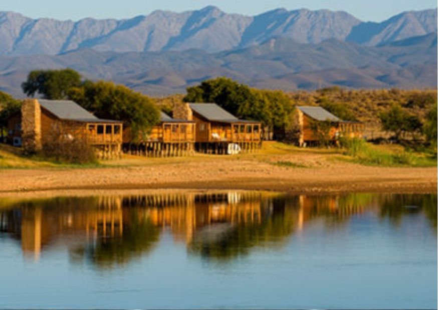 A view of DeZeekoe cottages with lake in foreground and mountains in background