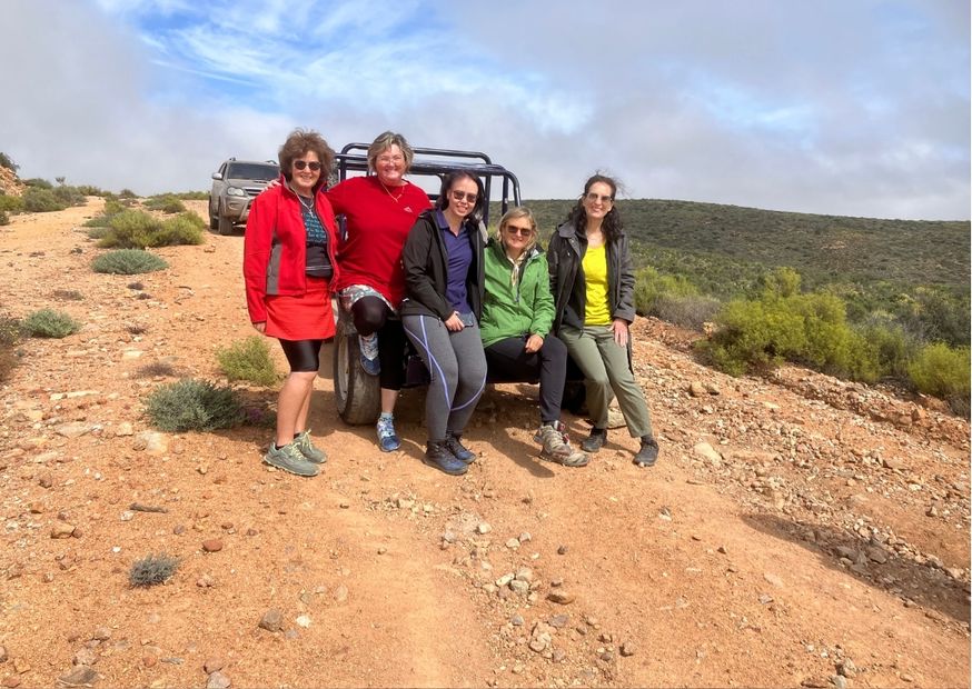 A group of 5 women-on-safari ladies sitting on a pip car facing the camera smiling. In Namaqualand.  