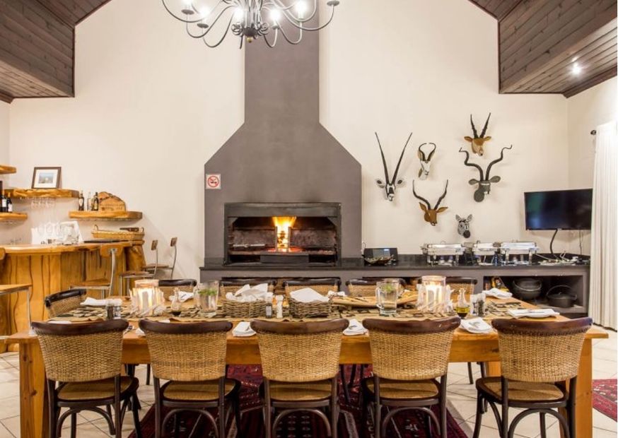 Inside the Wildehondkoof dining room table is laid and there is a fire burning in the fireplace in the background