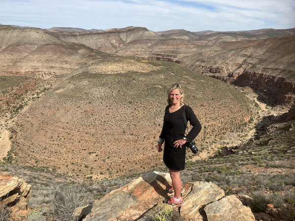 Woman standing on a rock looking at camera with camera over shoulder - the vast Schaap River Canyon (Namaqualand) is in the background. 