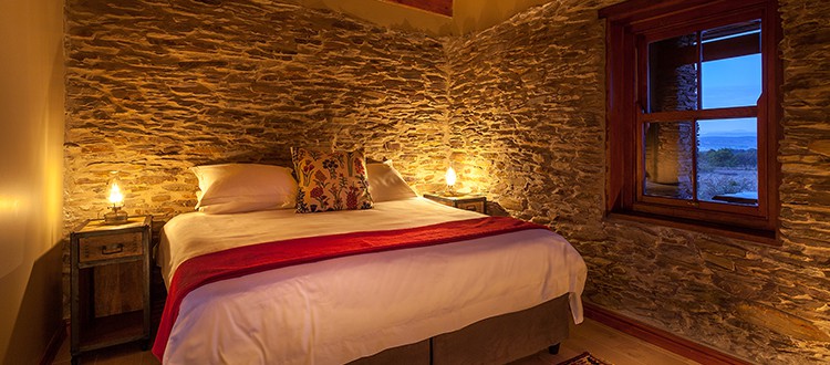 Looking into a cosy guest room at De Zeekoe Guest Farm double bed, stone walls and soft lighting
